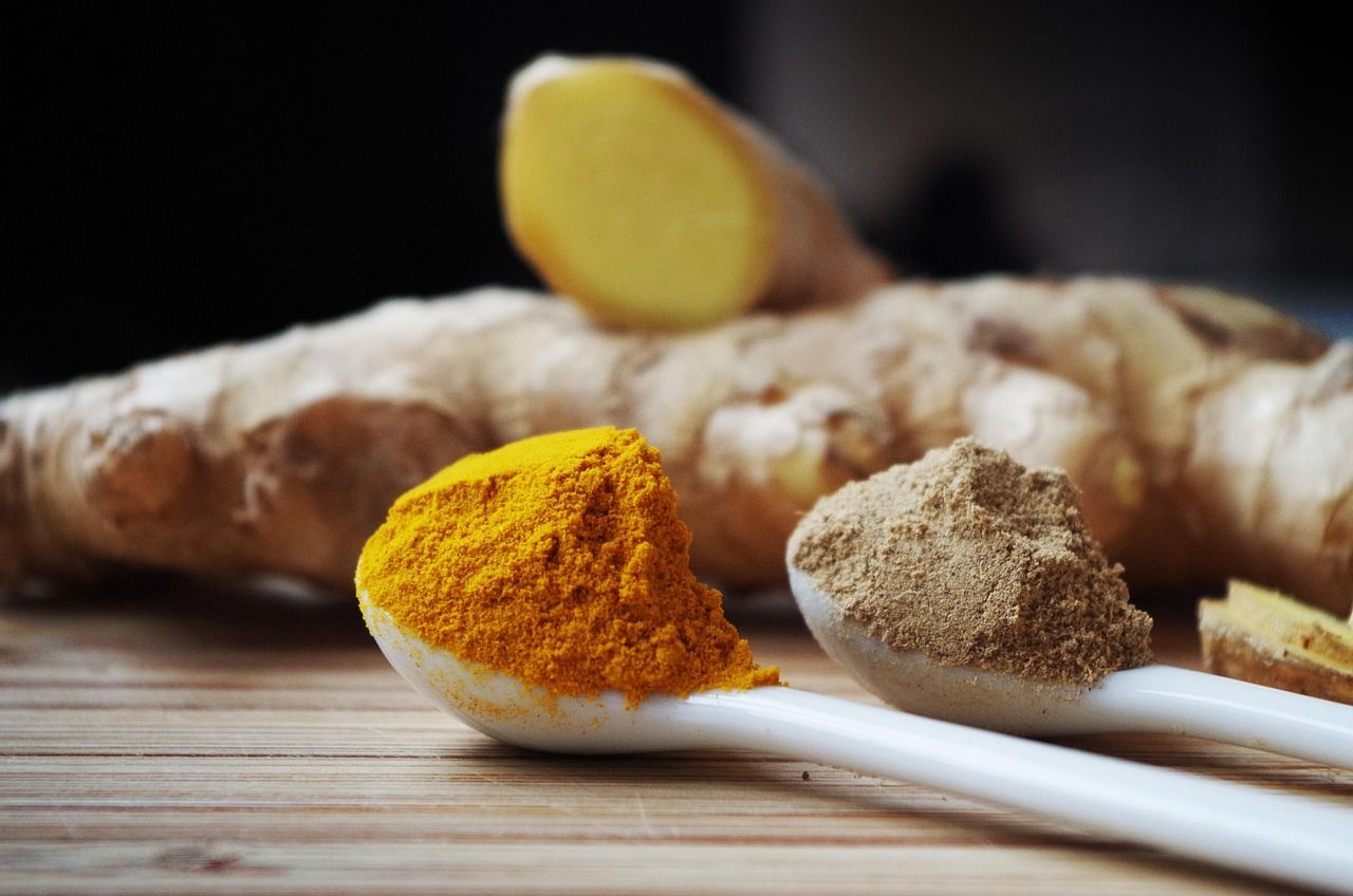 Fresh turmeric and ginger roots beside a spoon of orange turmeric powder on a wooden board