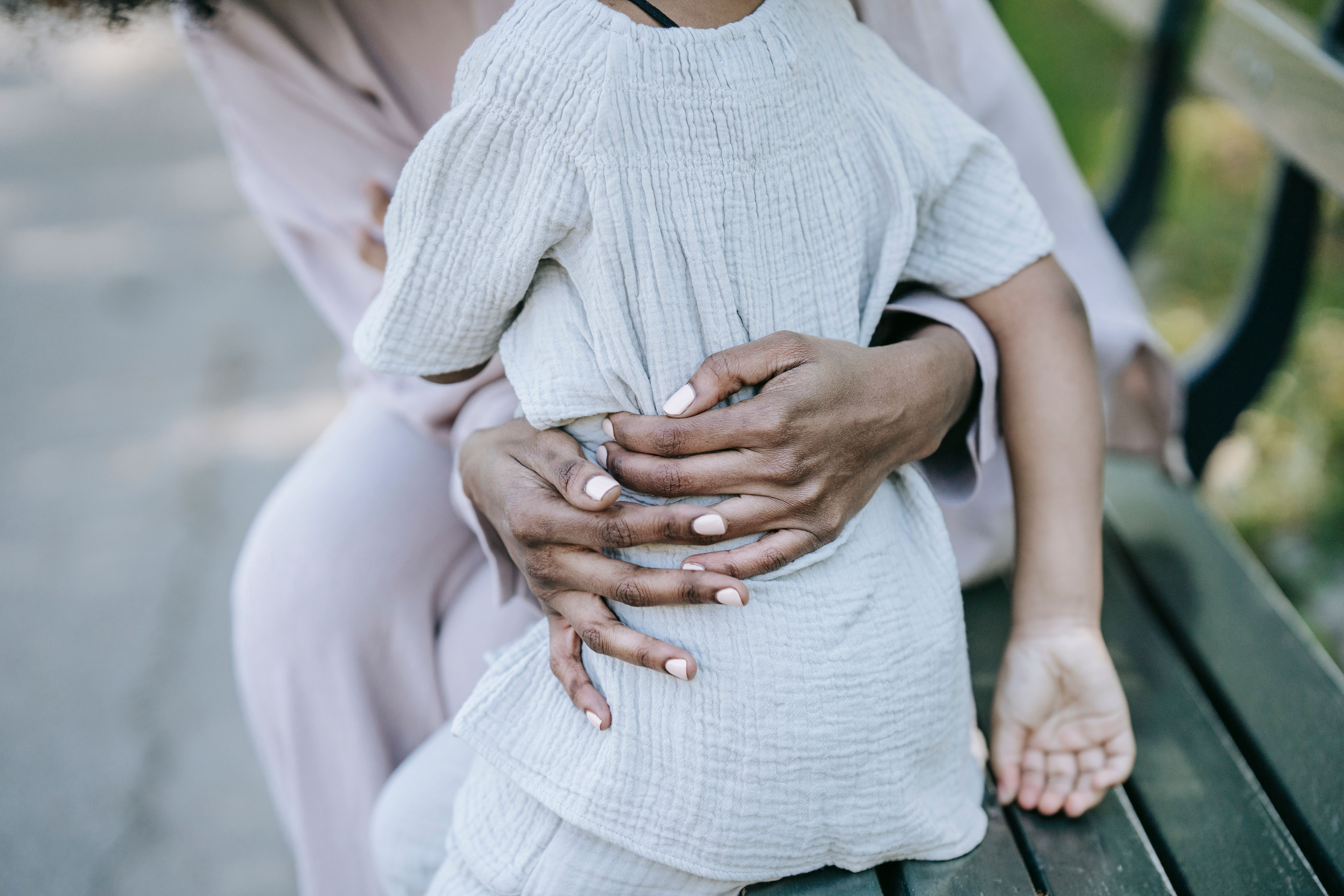 An adult tenderly embracing a child's hands outdoors, symbolizing protection and family reunion.