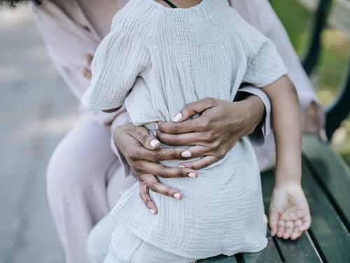 An adult tenderly embracing a child's hands outdoors, symbolizing protection and family reunion.