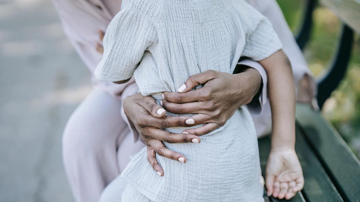 An adult tenderly embracing a child's hands outdoors, symbolizing protection and family reunion.