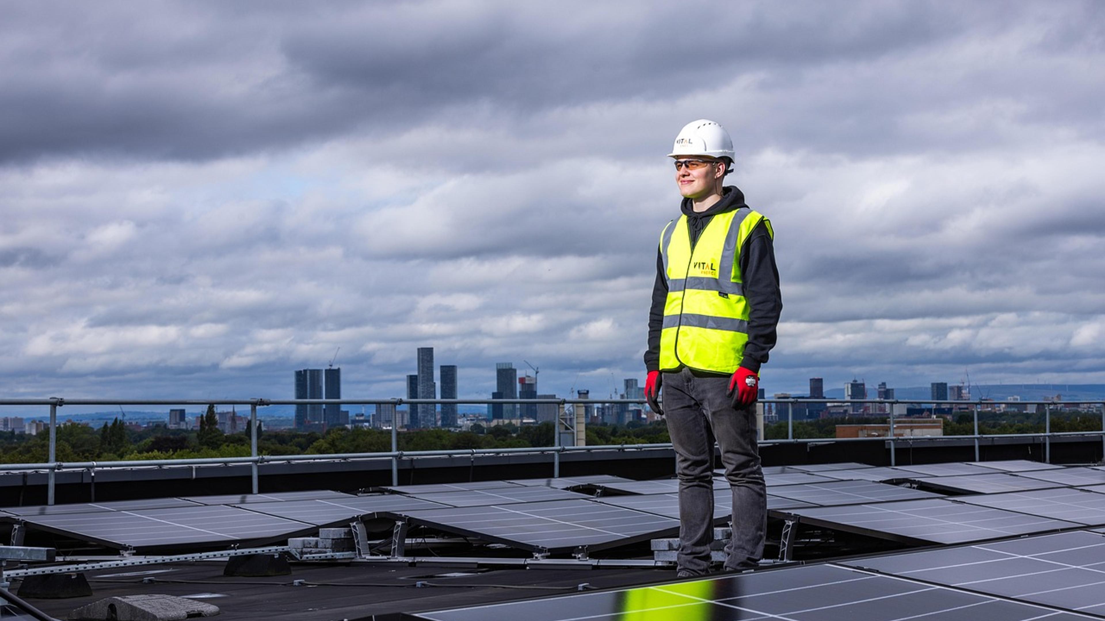 A worker in a hard hat and high-visibility vest standing among rooftop solar panels