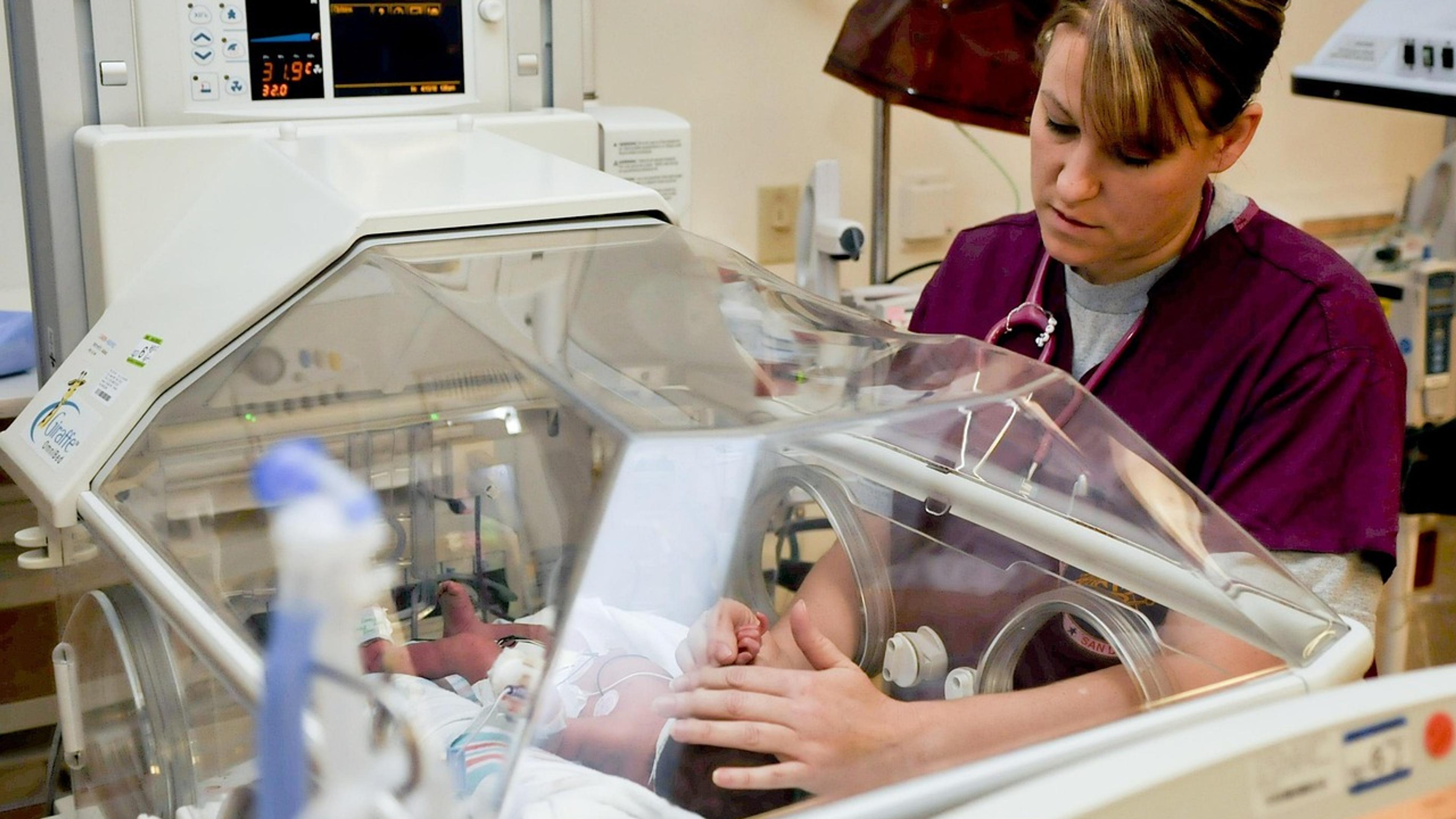 A nurse tending to a baby inside a hospital incubator