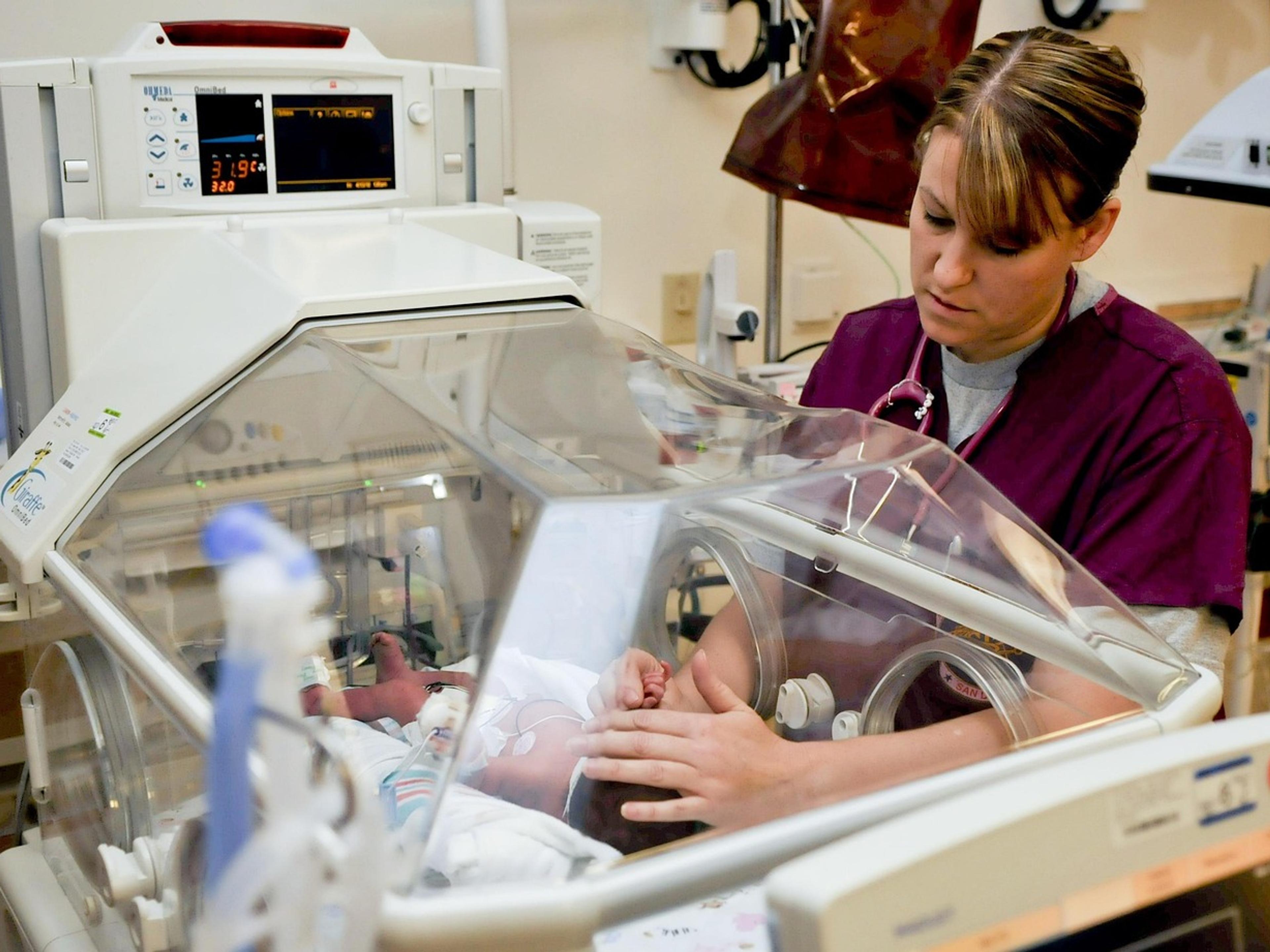 A nurse tending to a baby inside a hospital incubator