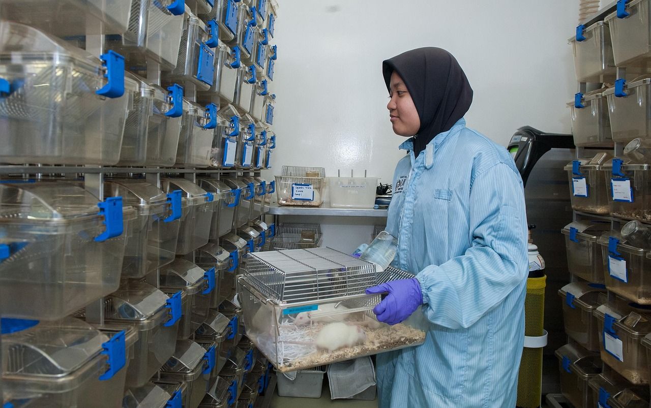 A researcher in a lab coat and gloves working at shelves of animal cages in a laboratory