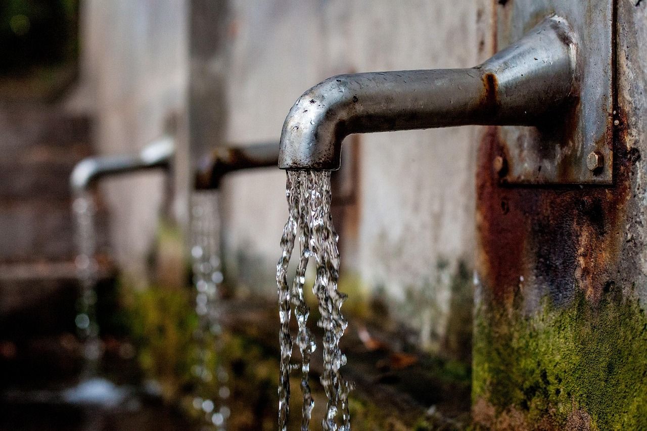 Water flowing from a metal tap on an outdoor wall