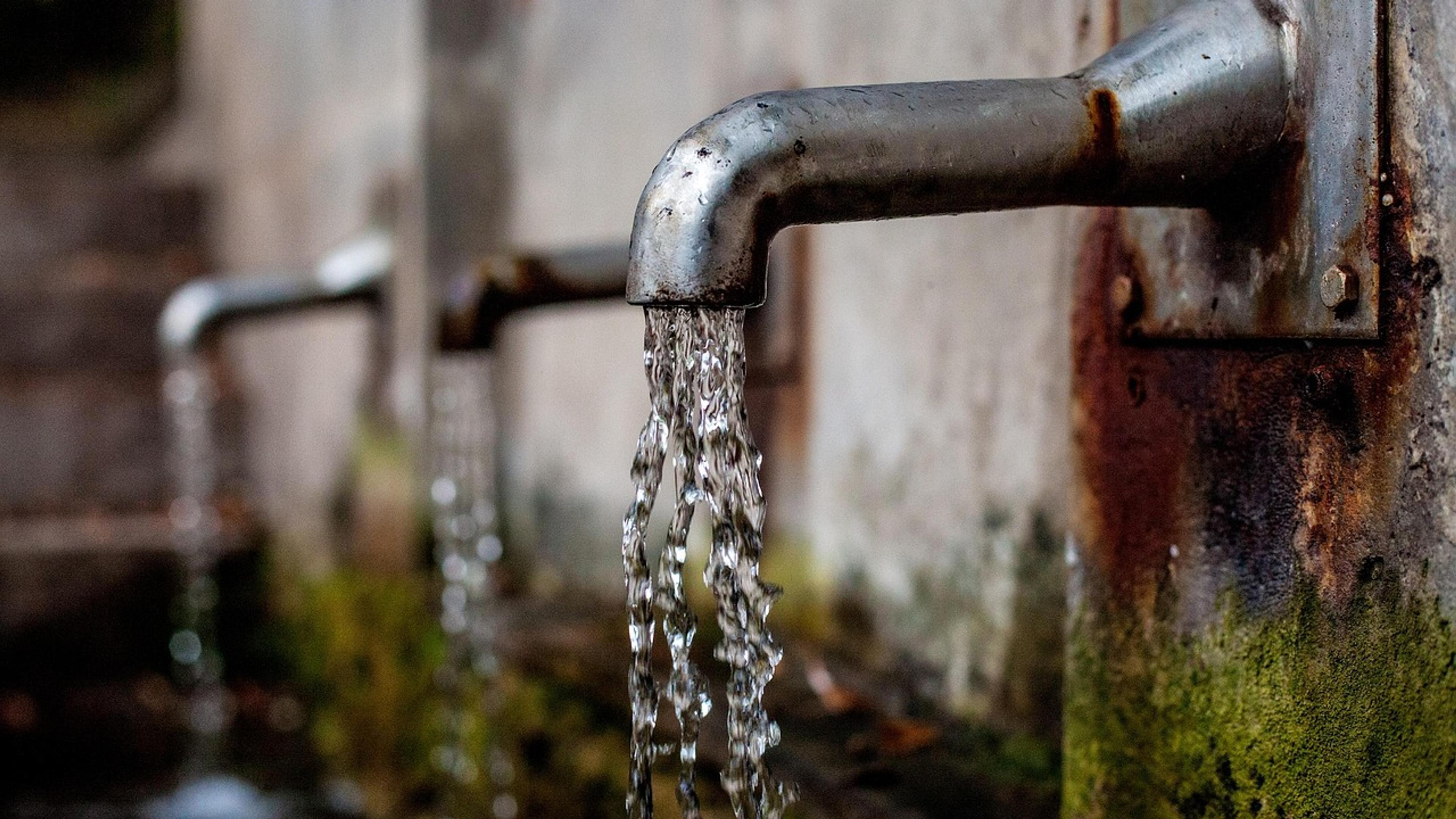 Water flowing from a metal tap on an outdoor wall