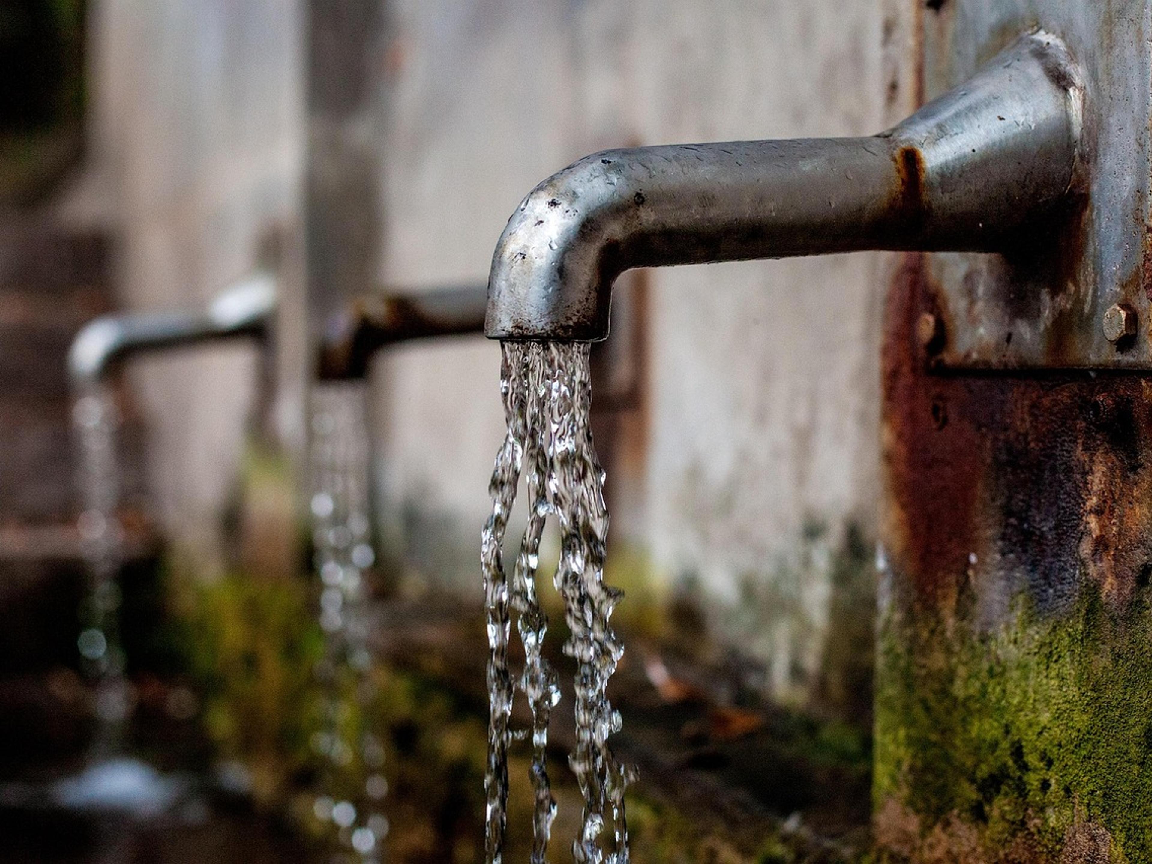 Water flowing from a metal tap on an outdoor wall
