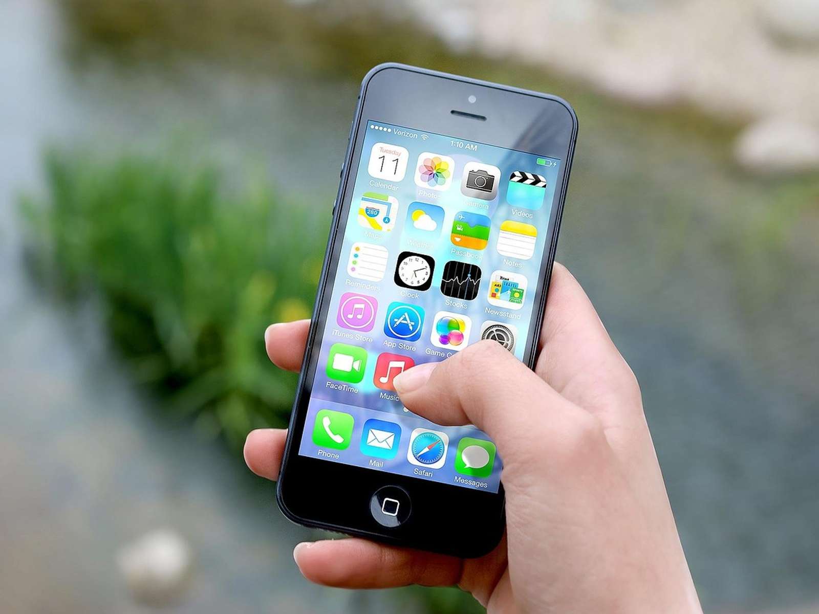 A hand holding a smartphone showing its home screen outdoors