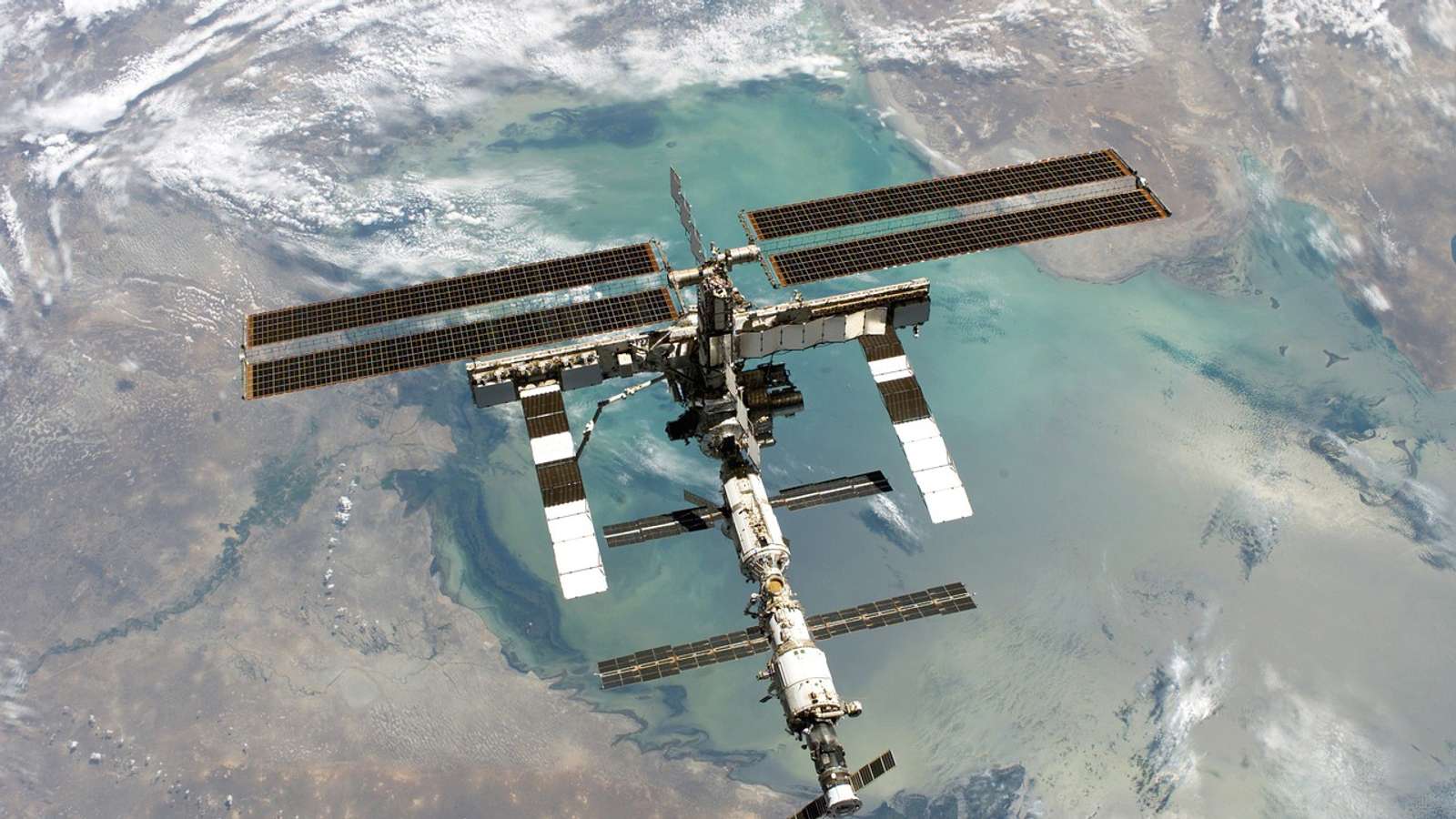 The International Space Station with its solar arrays extended, seen from above against the Earth