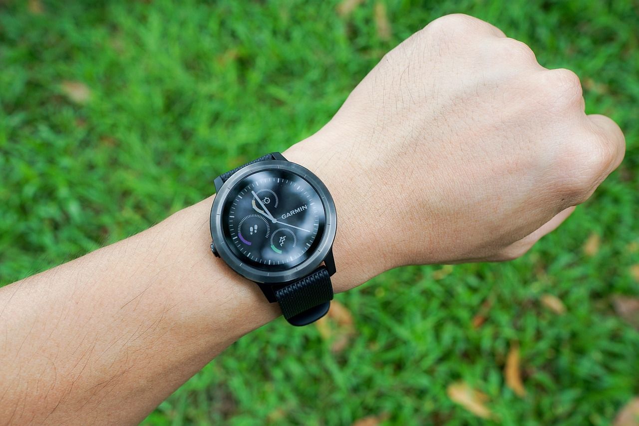 A person's wrist wearing a black smartwatch above green grass