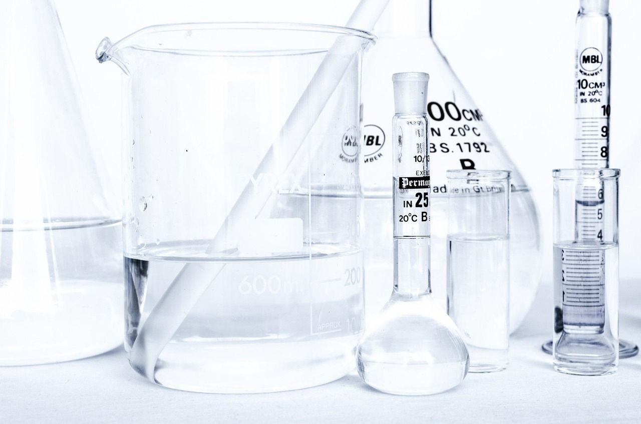 Clear laboratory glassware, including beakers, flasks and measuring cylinders, on a white bench
