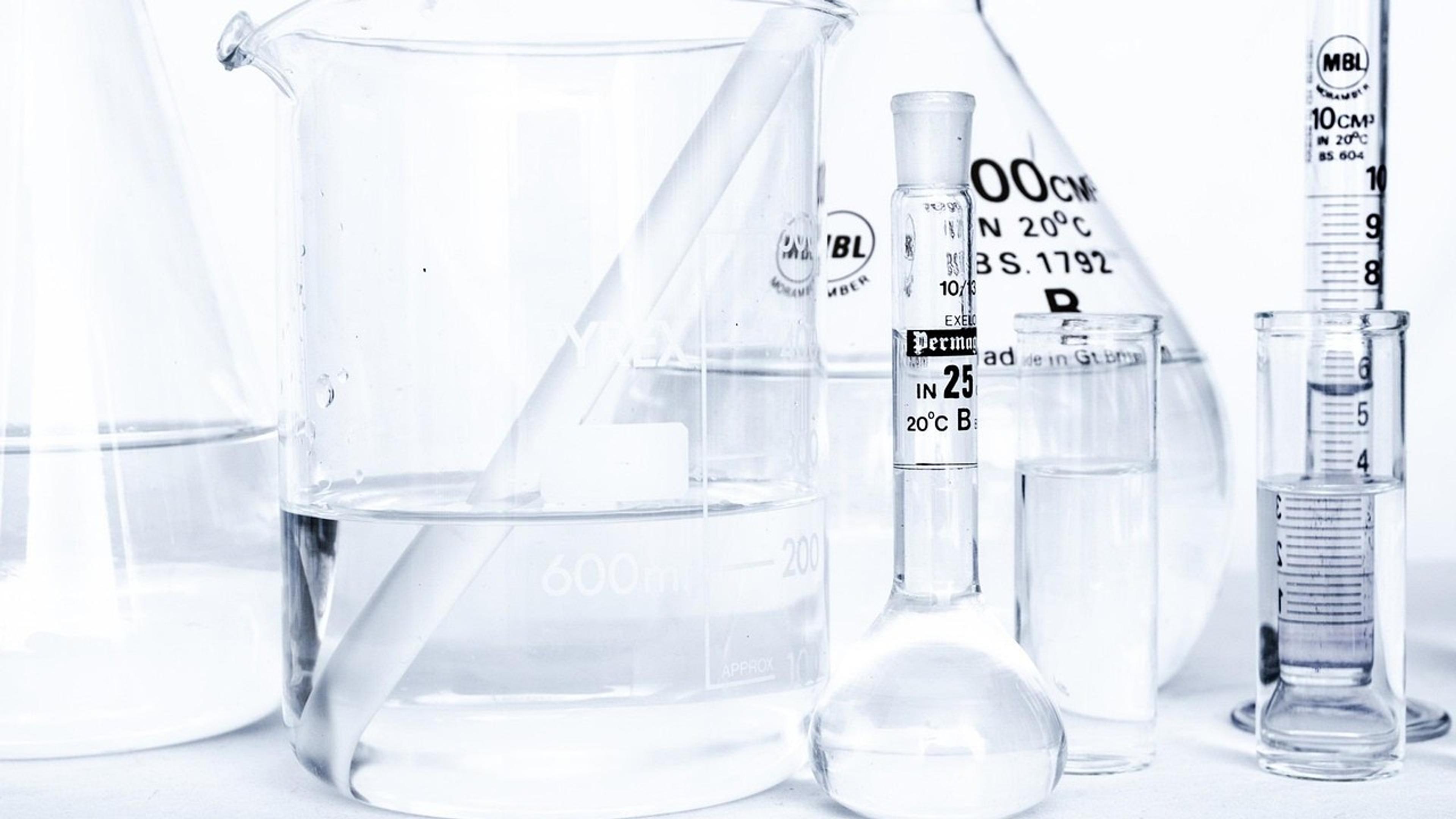Clear laboratory glassware, including beakers, flasks and measuring cylinders, on a white bench