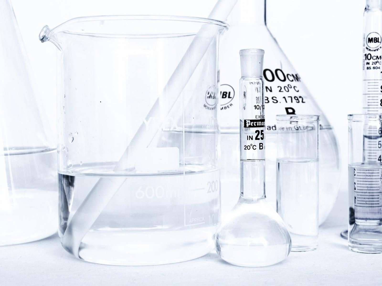 Clear laboratory glassware, including beakers, flasks and measuring cylinders, on a white bench