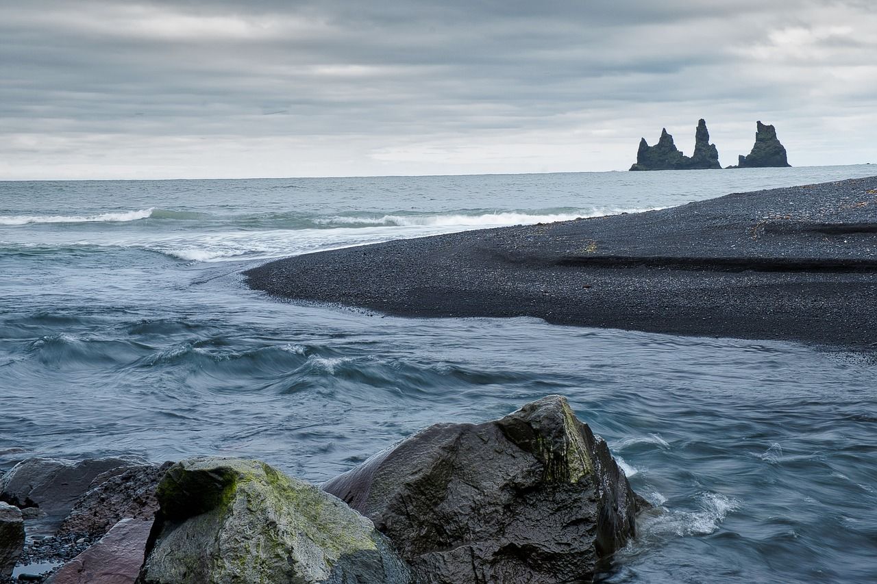 Grey North Atlantic waves washing onto a black sand beach in Iceland under cloudy skies