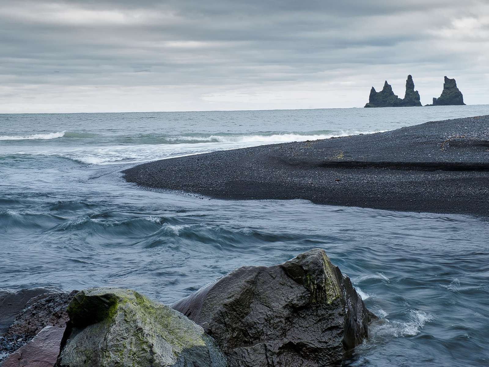 Grey North Atlantic waves washing onto a black sand beach in Iceland under cloudy skies