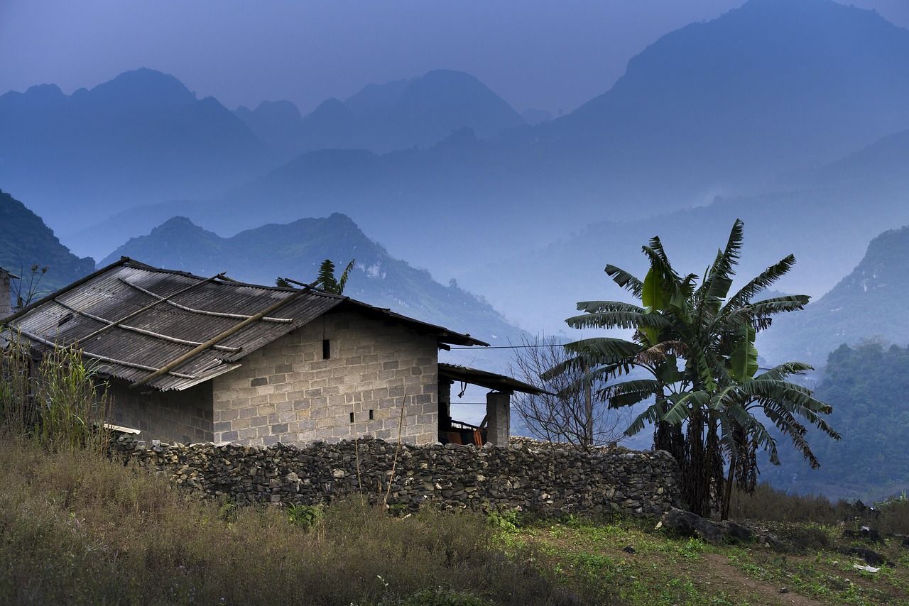 A small brick house with a corrugated roof and a banana tree in front of misty mountains in Ha Giang, northern Vietnam