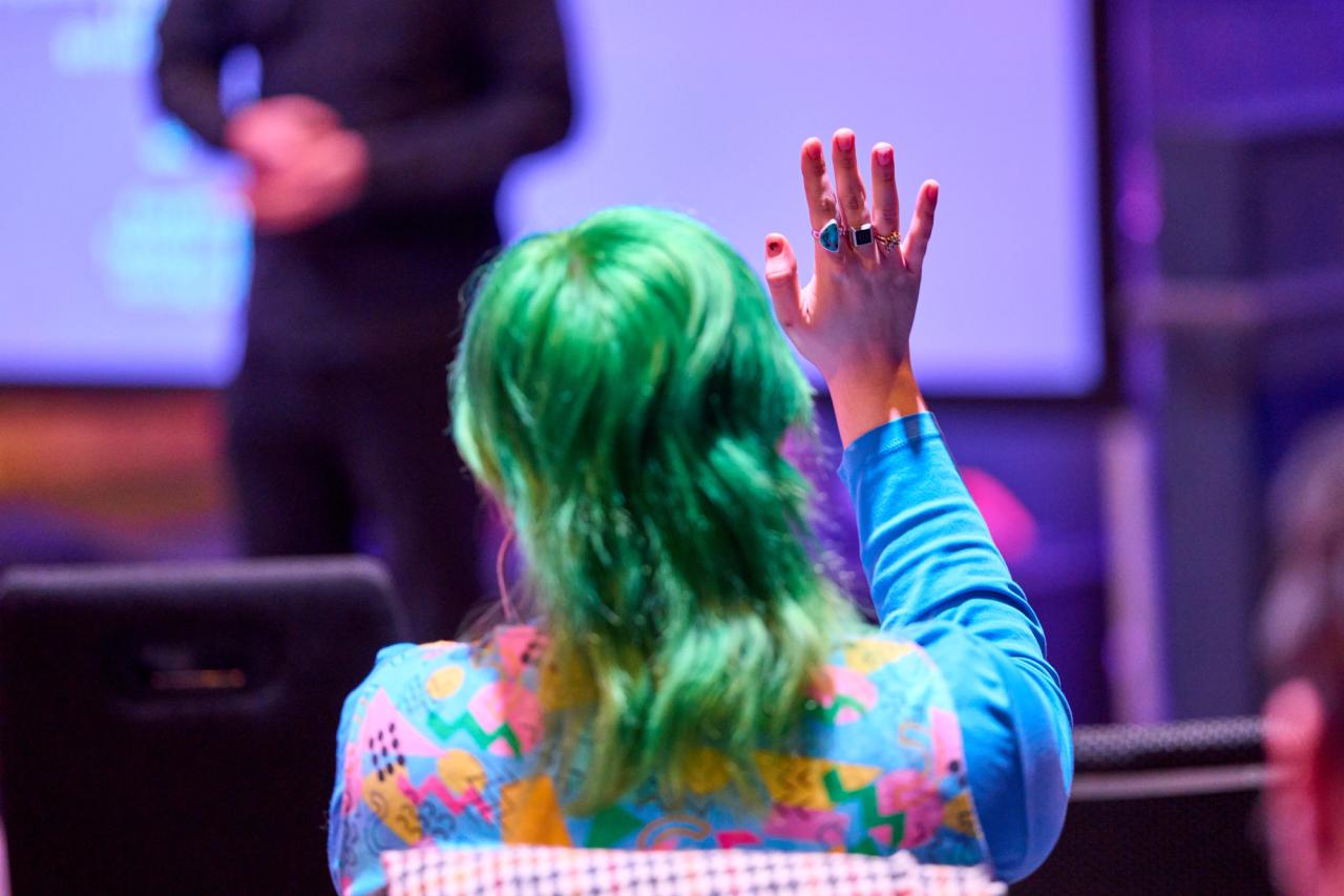 A woman in the audience with green hair raising her hand.
