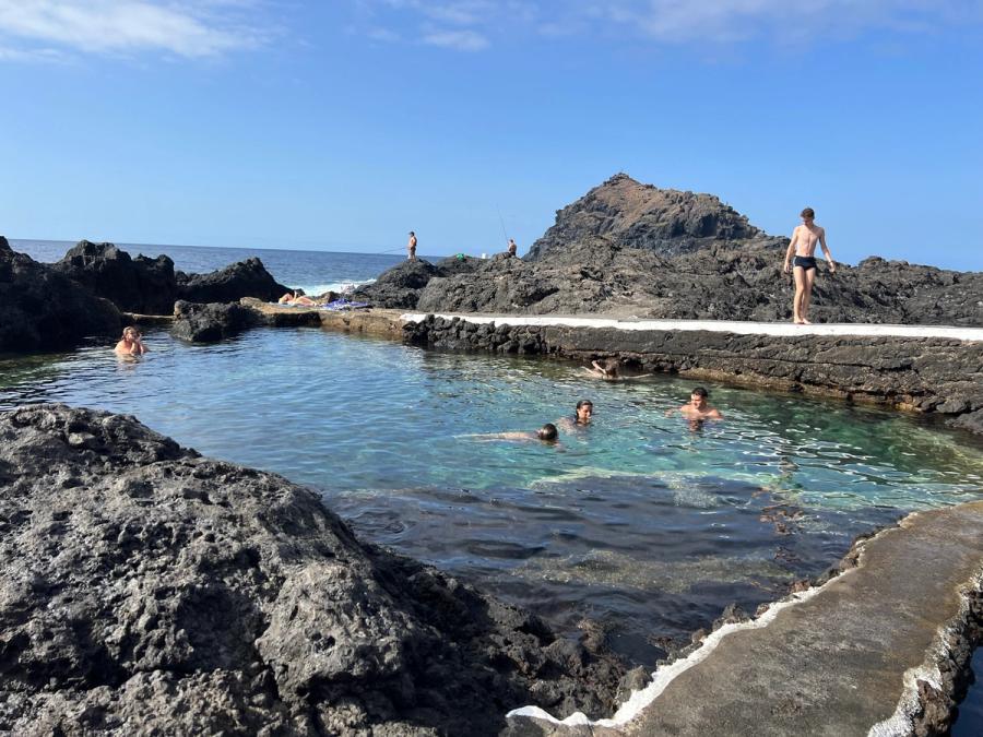 Bañistas nadando en una poza de El Caletón de Garachico, con el borde encalado sobre la lava negra y el mar detrás.