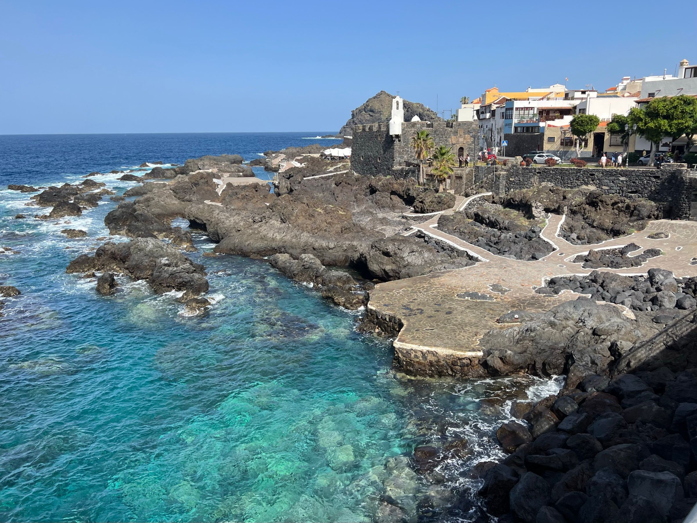 El agua turquesa de las piscinas naturales de El Caletón, en Garachico, entre la roca volcánica y con las casas del pueblo al fondo.