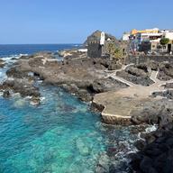 El agua turquesa de las piscinas naturales de El Caletón, en Garachico, entre la roca volcánica y con las casas del pueblo al fondo.