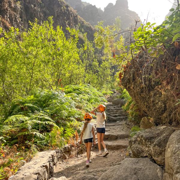 Dos niñas con casco naranja suben por el sendero escalonado del Barranco del Infierno, entre helechos y paredes de roca