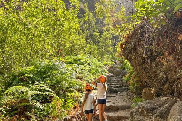 Dos niñas con casco naranja suben por el sendero escalonado del Barranco del Infierno, entre helechos y paredes de roca