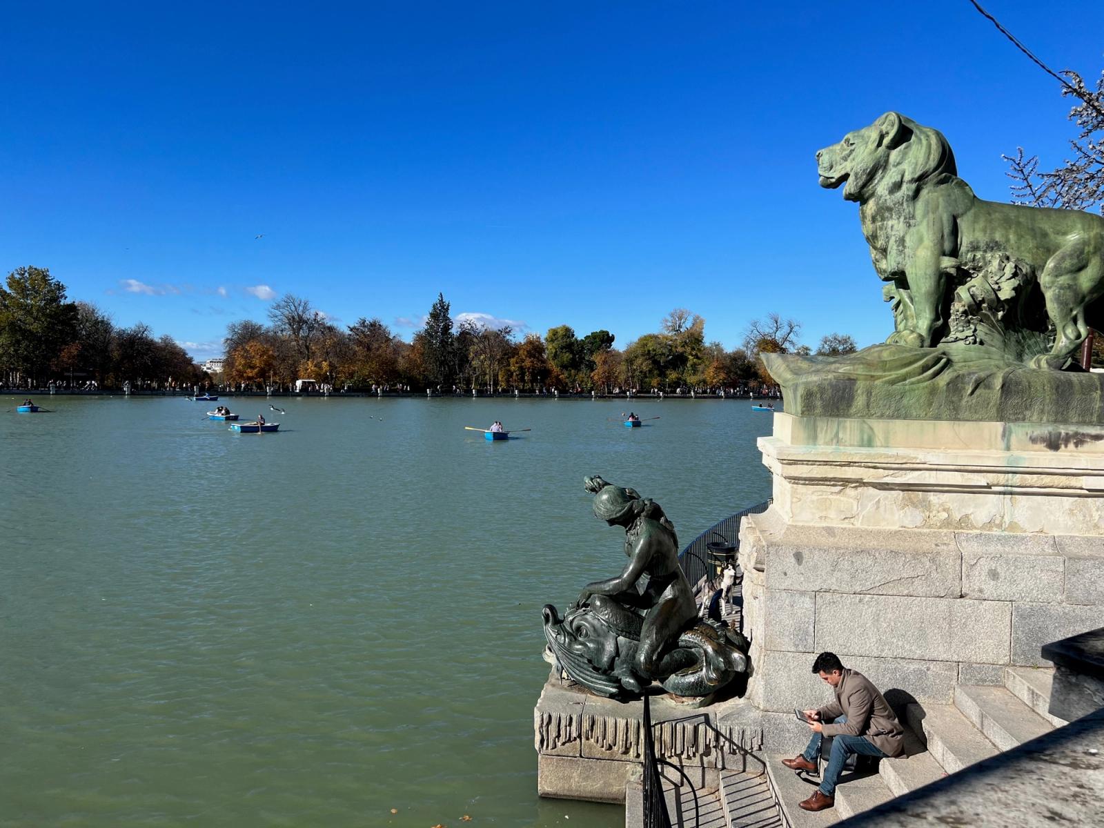 El monumento a Alfonso XII en el Retiro, con uno de sus leones de bronce y las barcas en el estanque al fondo.
