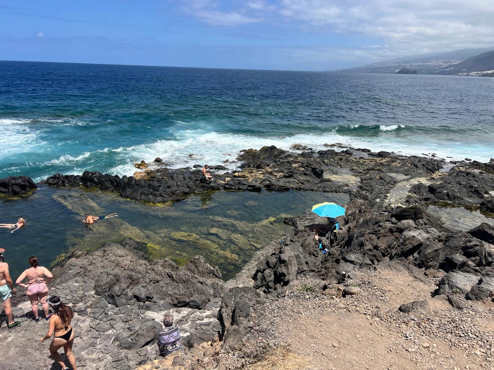 El Charco de los Chochos visto desde un lateral: la poza de agua transparente entre la roca volcánica y el mar abierto rompiendo fuera.