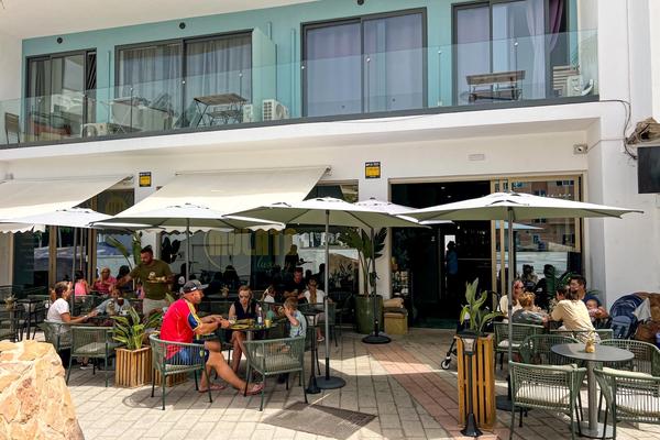 Terraza de MULATA Luxury Café en Corralejo (Fuerteventura), con mesas verdes bajo sombrillas blancas, clientes desayunando y la fachada del local al fondo.