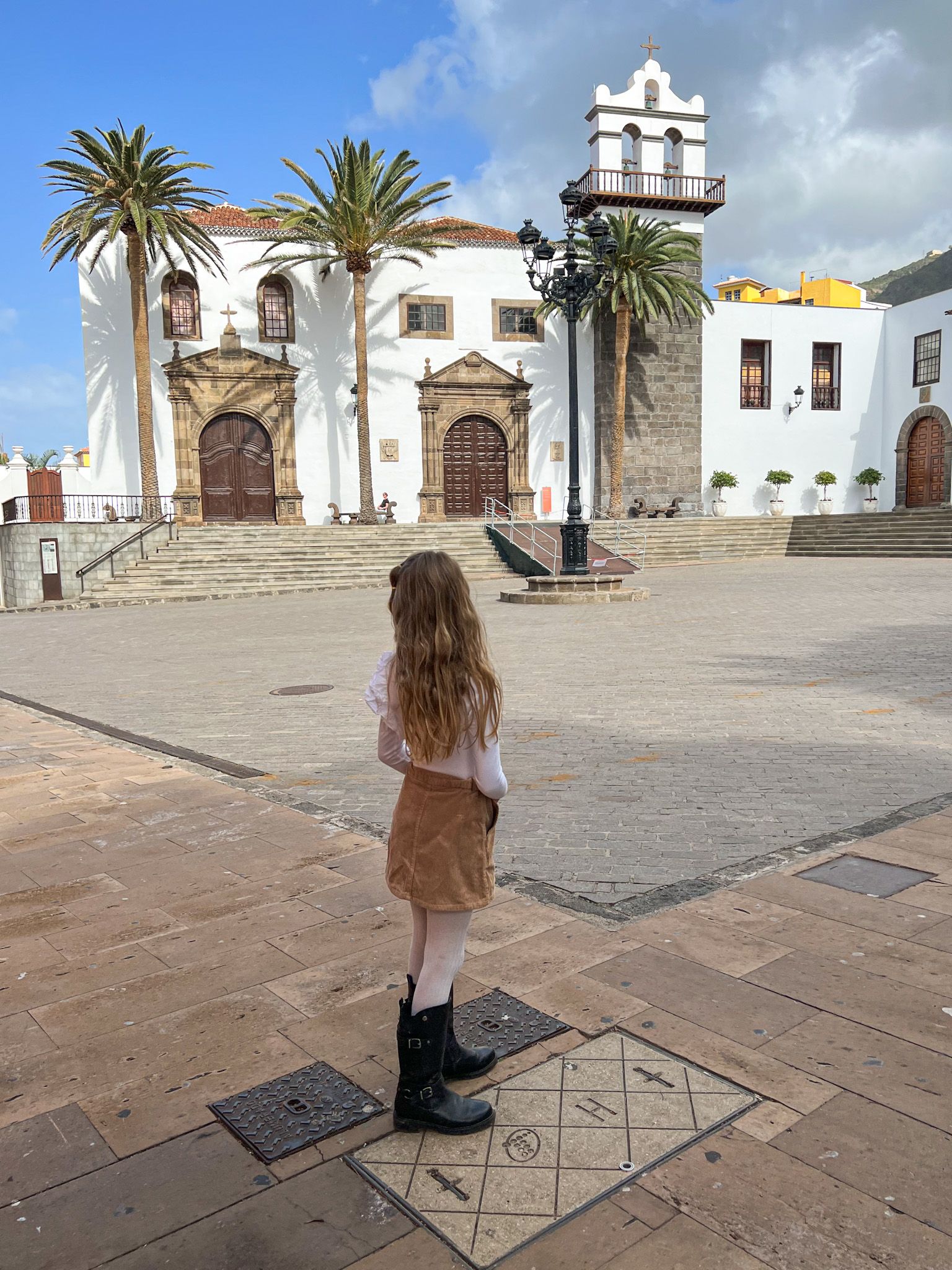 Una niña en la Plaza de la Libertad de Garachico mirando el antiguo Convento de San Francisco, con sus palmeras y la espadaña blanca.