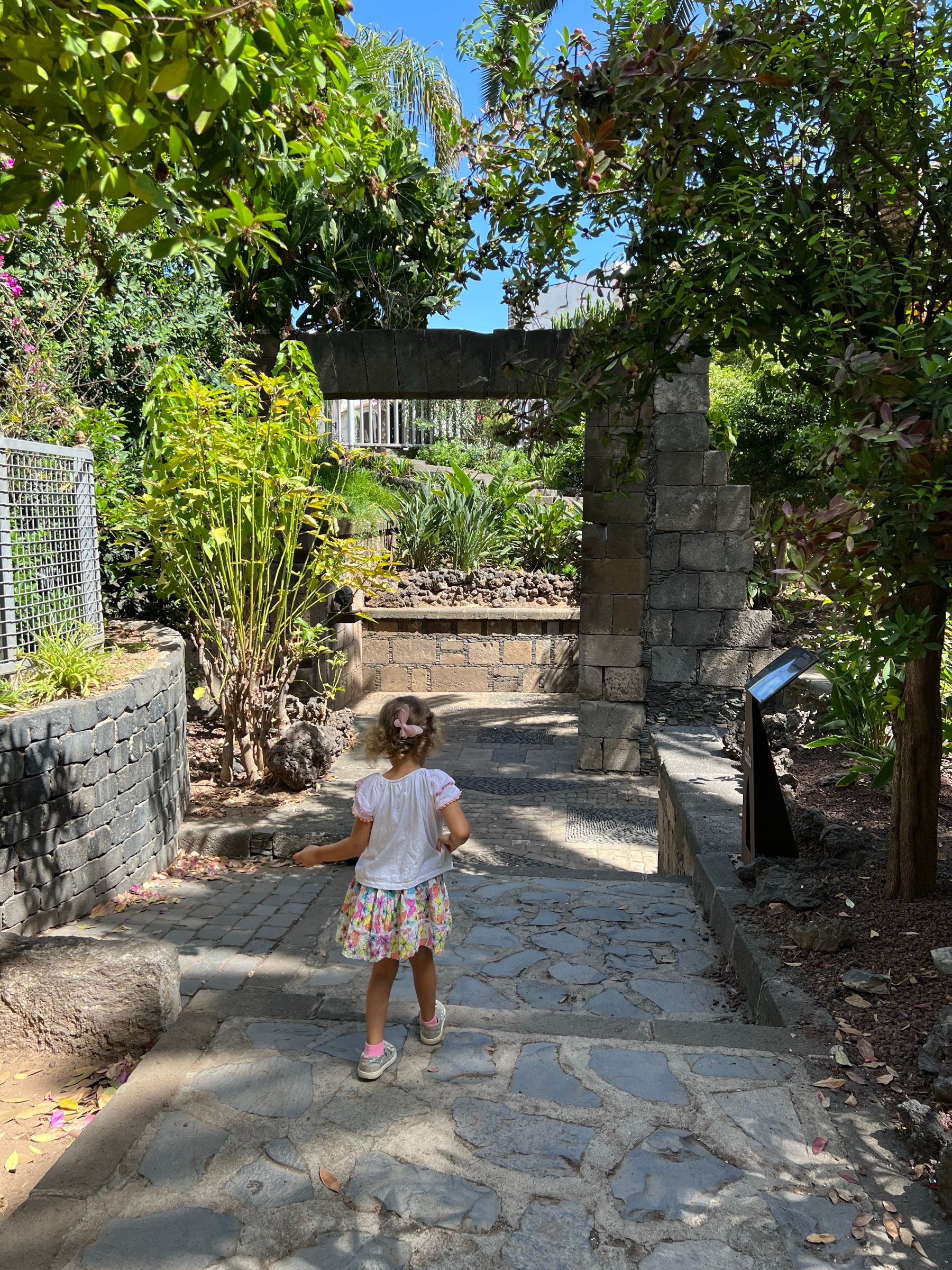 Una niña camina hacia el arco de piedra de la Puerta de Tierra, entre los jardines del parque, en Garachico.