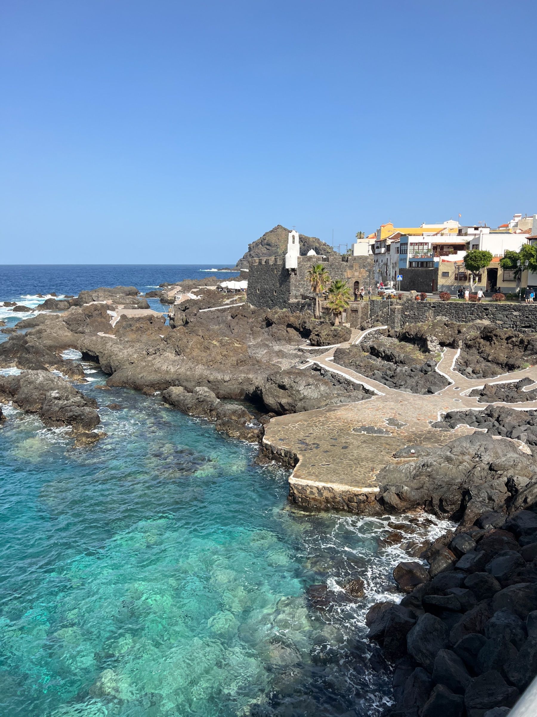 Las piscinas naturales de El Caletón en Garachico, con el agua turquesa entre la roca volcánica, el Castillo de San Miguel y las casas del pueblo al fondo.