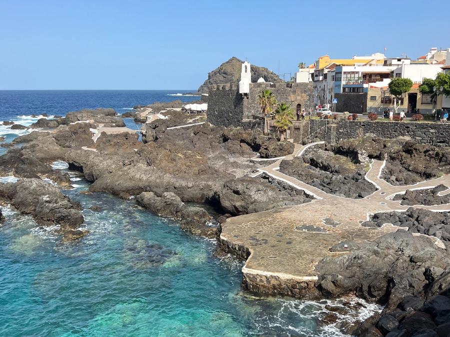 Las piscinas naturales de El Caletón en Garachico, con el agua turquesa entre la roca volcánica, el Castillo de San Miguel y las casas del pueblo al fondo.