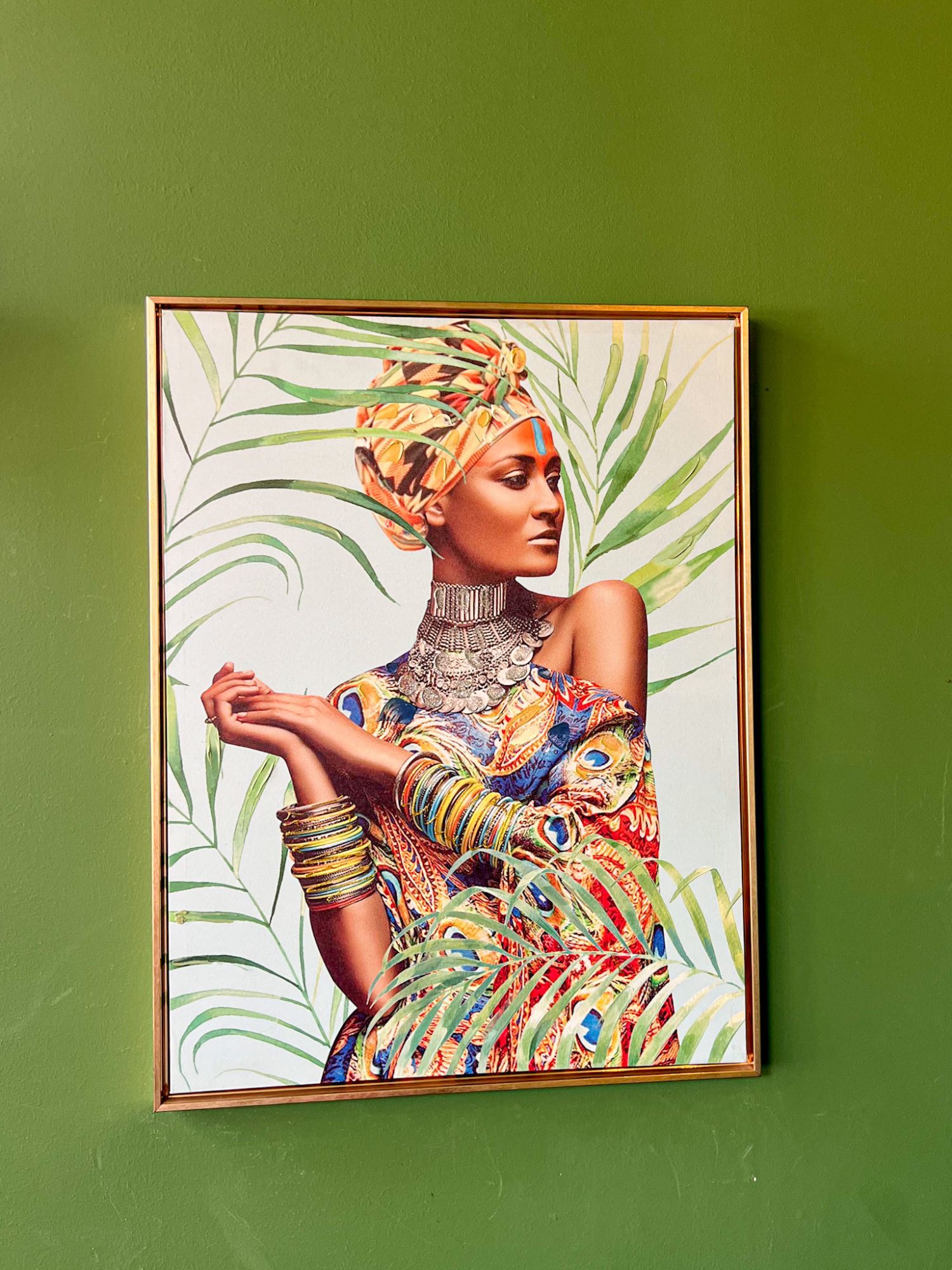 A gold-framed picture on MULATA's green wall, showing a woman in a colourful turban among palm leaves.