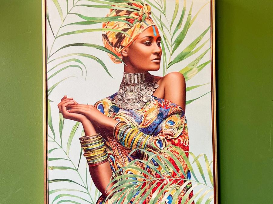 A gold-framed picture on MULATA's green wall, showing a woman in a colourful turban among palm leaves.