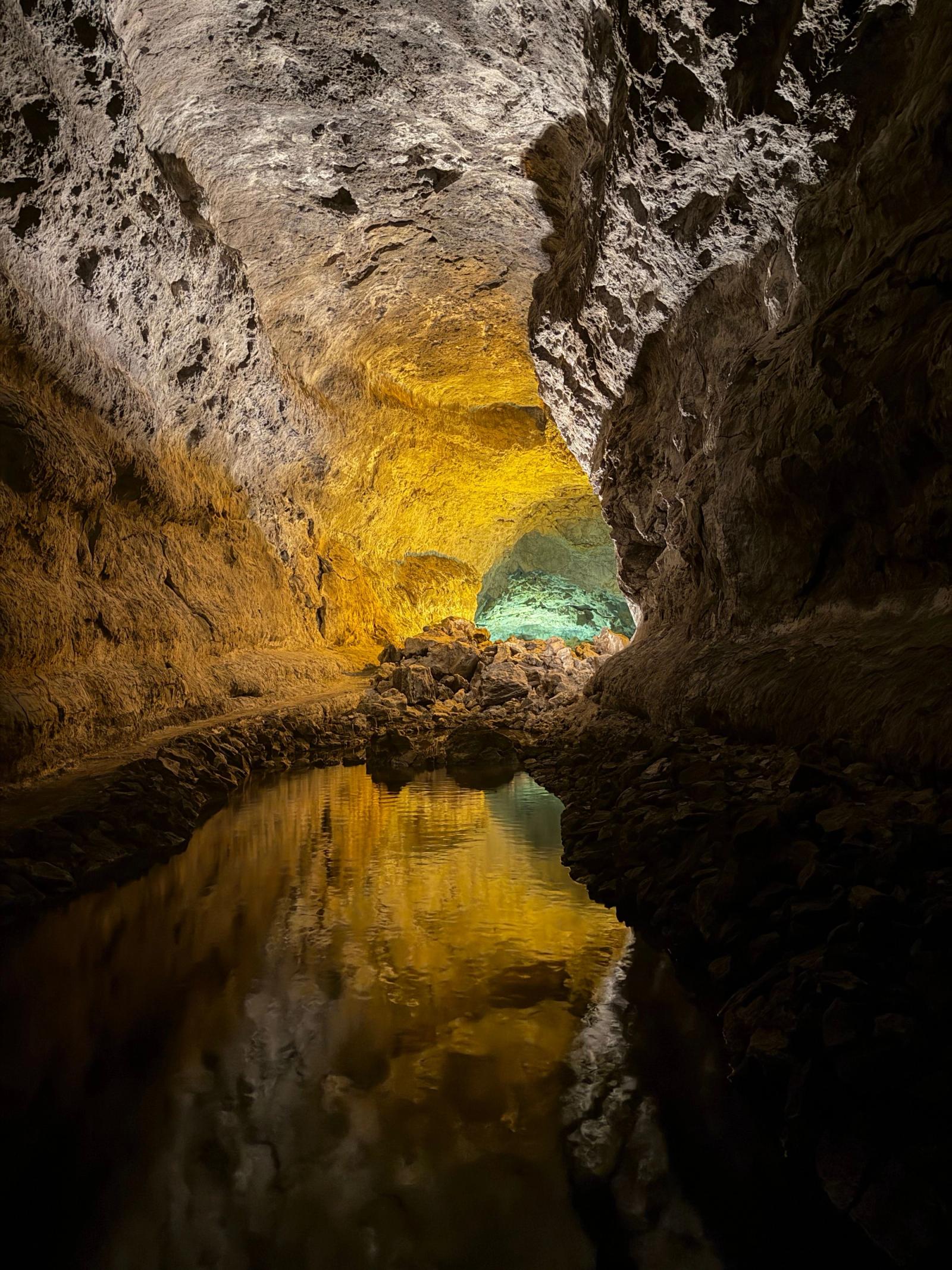 Interior de la Cueva de los Verdes, con las paredes de lava iluminadas en dorado y reflejadas en una charca de agua