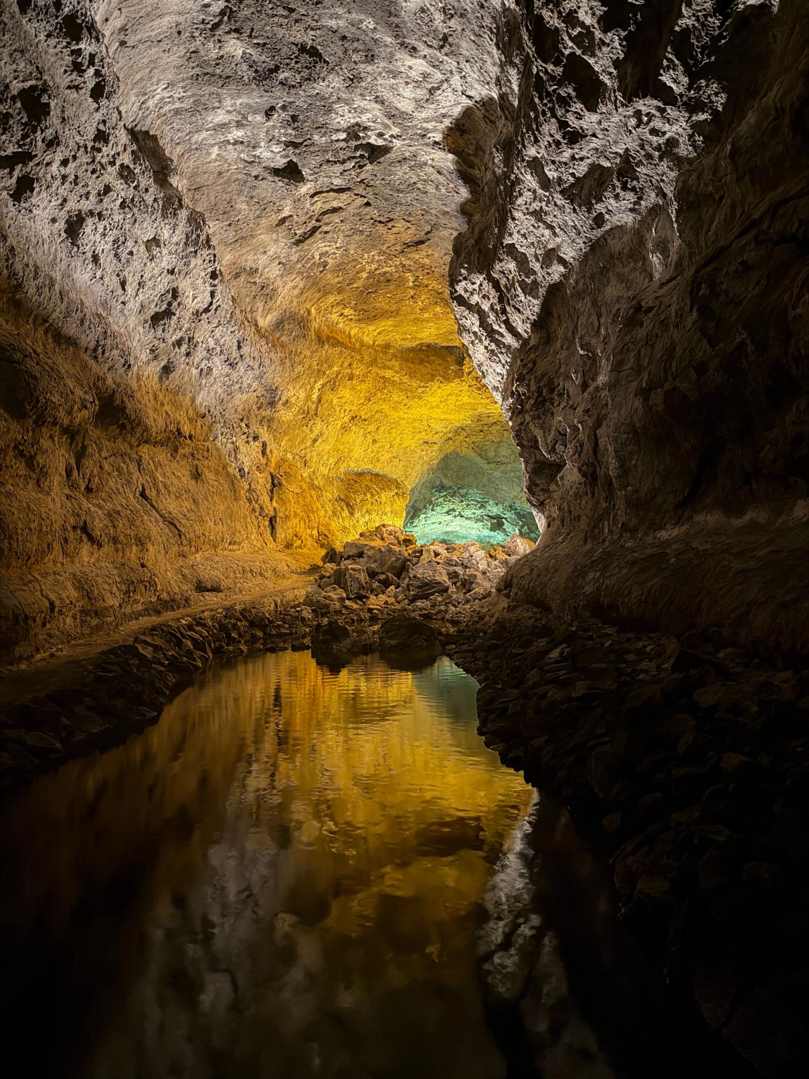 Interior de la Cueva de los Verdes, con las paredes de lava iluminadas en dorado y reflejadas en una charca de agua