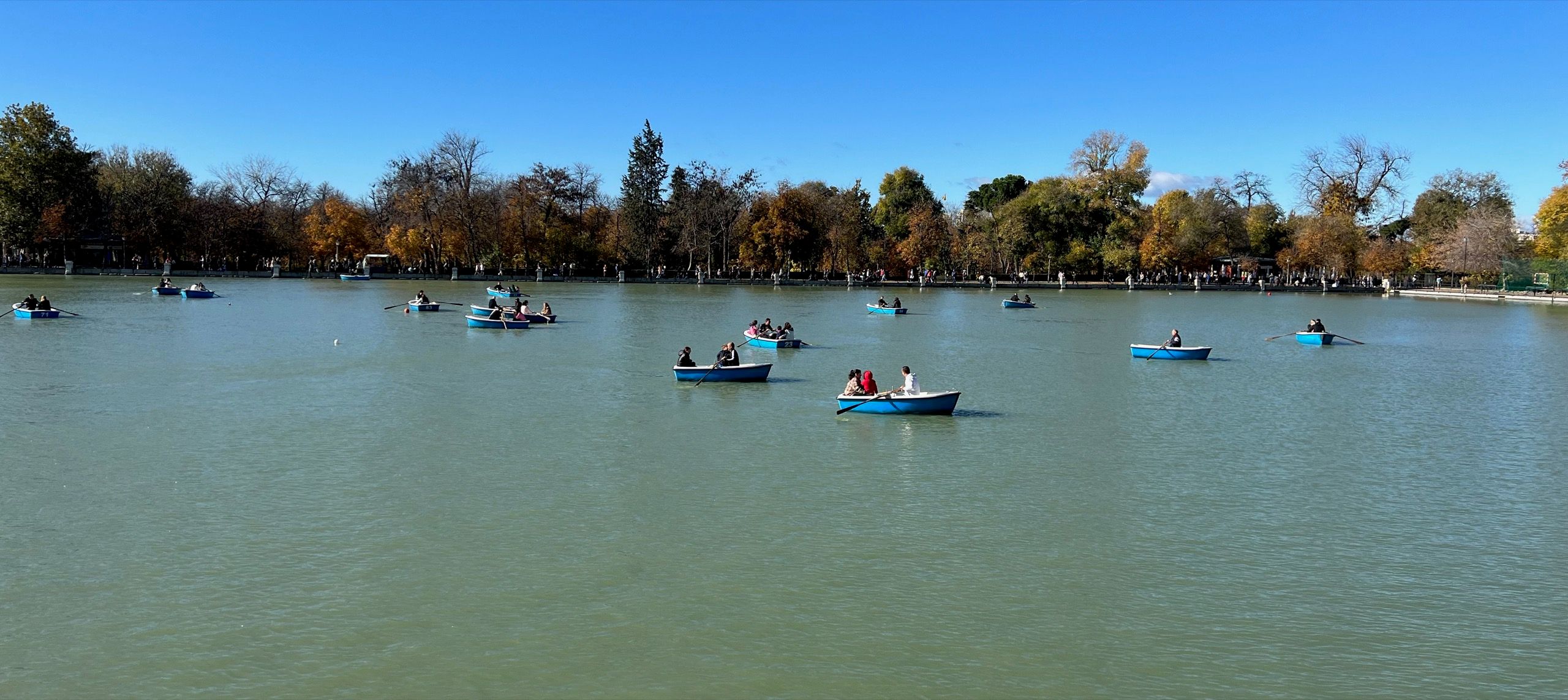 Barcas azules de remo en el Estanque Grande del Retiro, con los árboles en otoño al fondo.