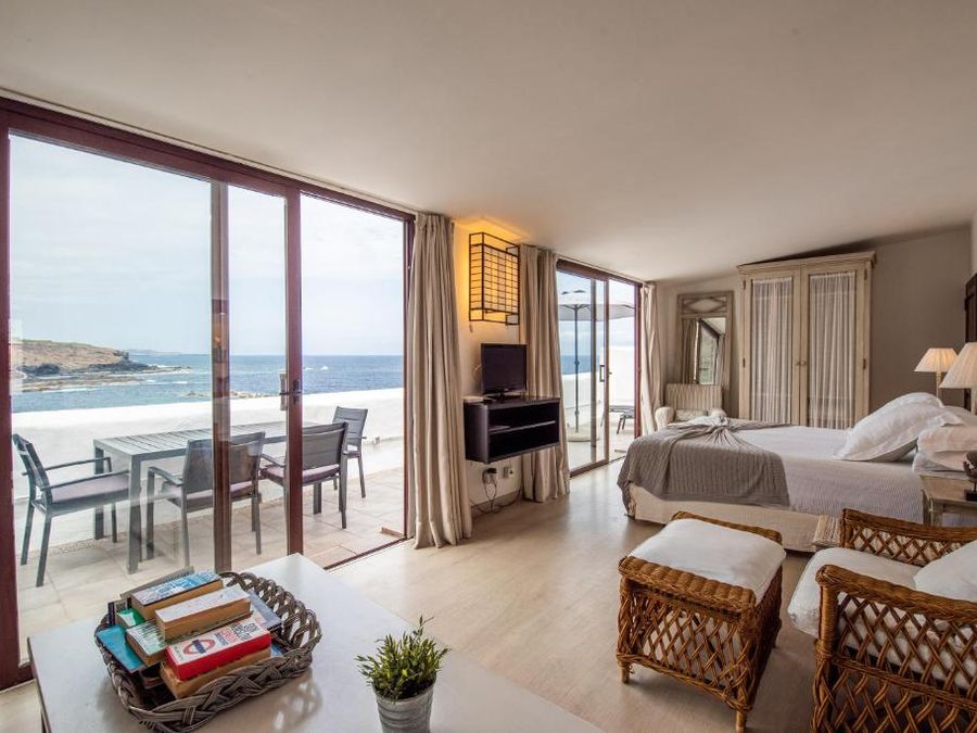 Suite de Isla Baja Suites con ventanales al Atlántico, terraza con mesa y sillas, y la cama al fondo.