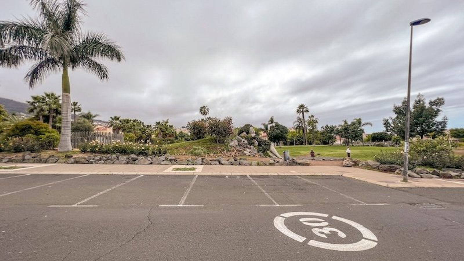 Plazas de aparcamiento libres junto al parque, con las rocas del jardín y las palmeras al fondo.