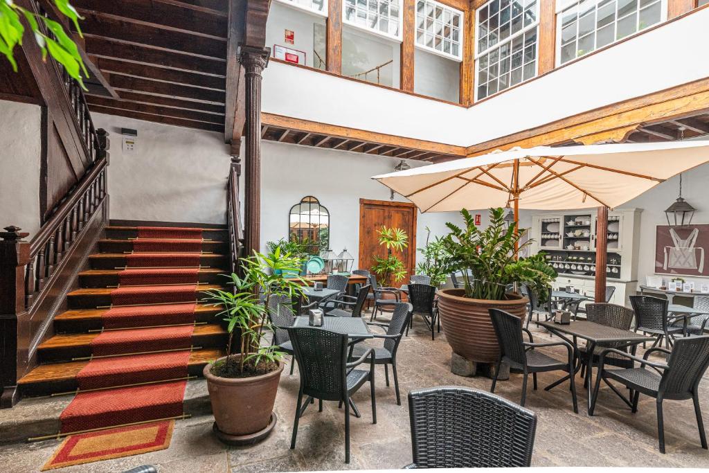 Patio interior de Isla Baja Suites, en Garachico: escalera de madera con alfombra roja, mesas bajo una sombrilla y plantas en macetas, en una casa canaria del siglo XVIII.