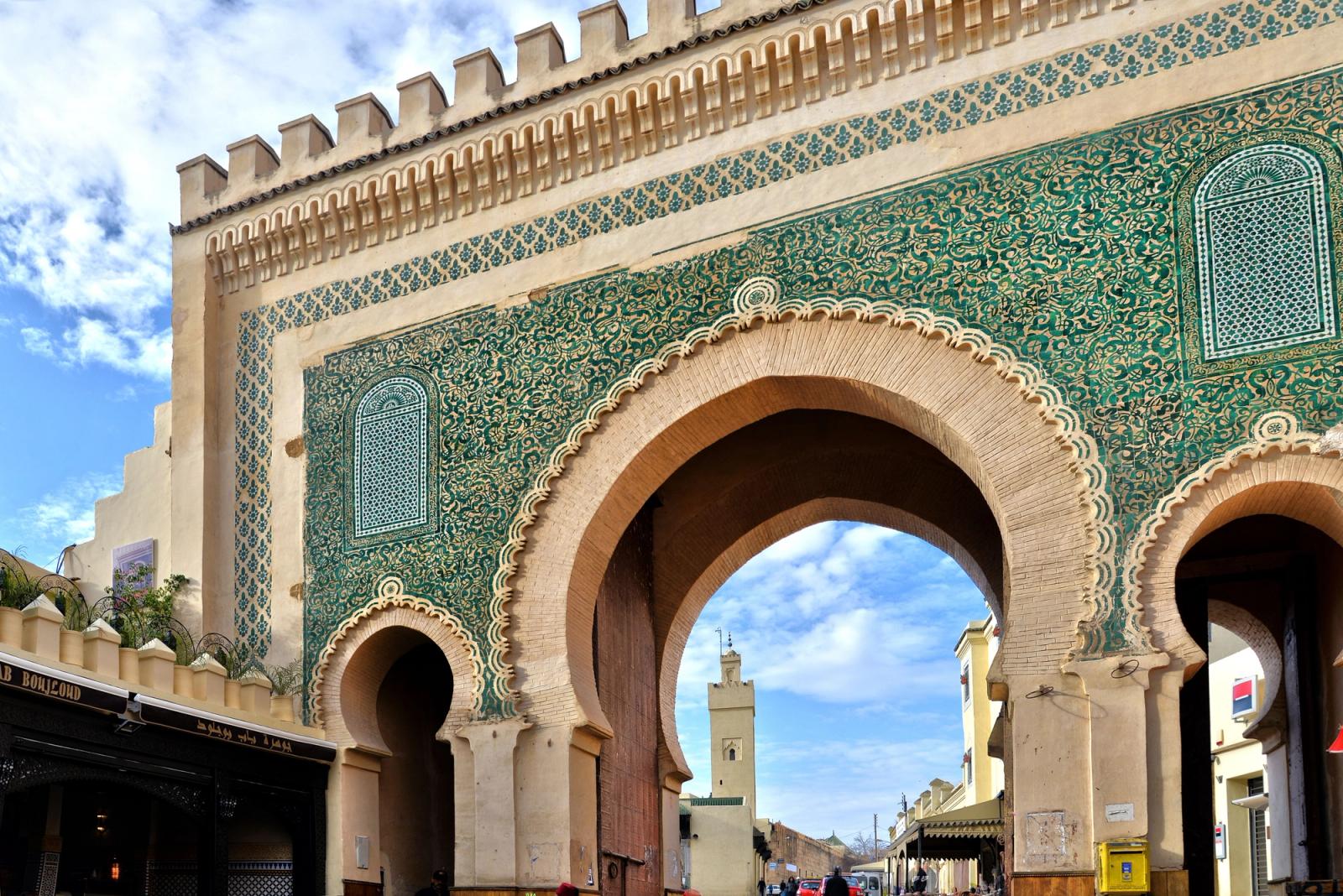 Puerta monumental de una medina marroquí, con azulejos verdes y un minarete al fondo