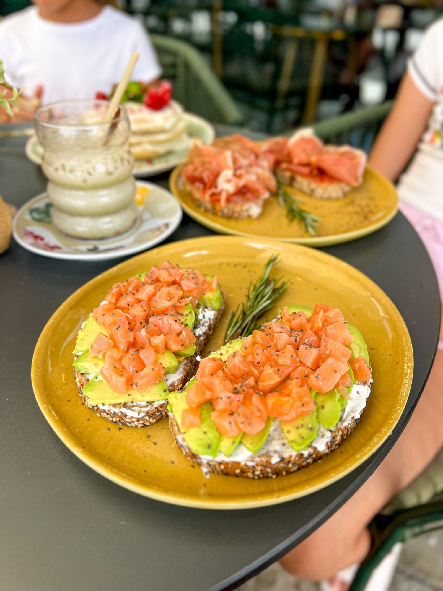 Salmon toast with avocado and cream cheese, served on wholegrain bread on a green plate on MULATA's terrace.
