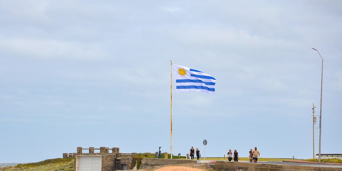 Uruguayan flag flying on a pole by the sea.