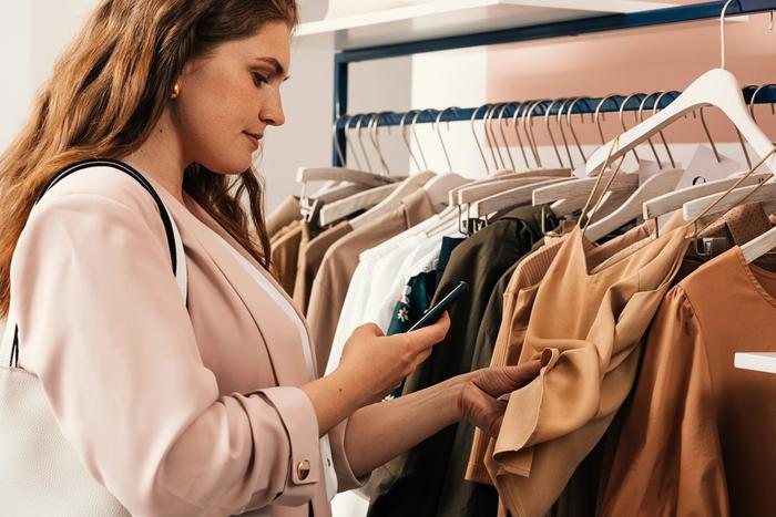 a woman is looking at her phone while shopping for clothes in a store