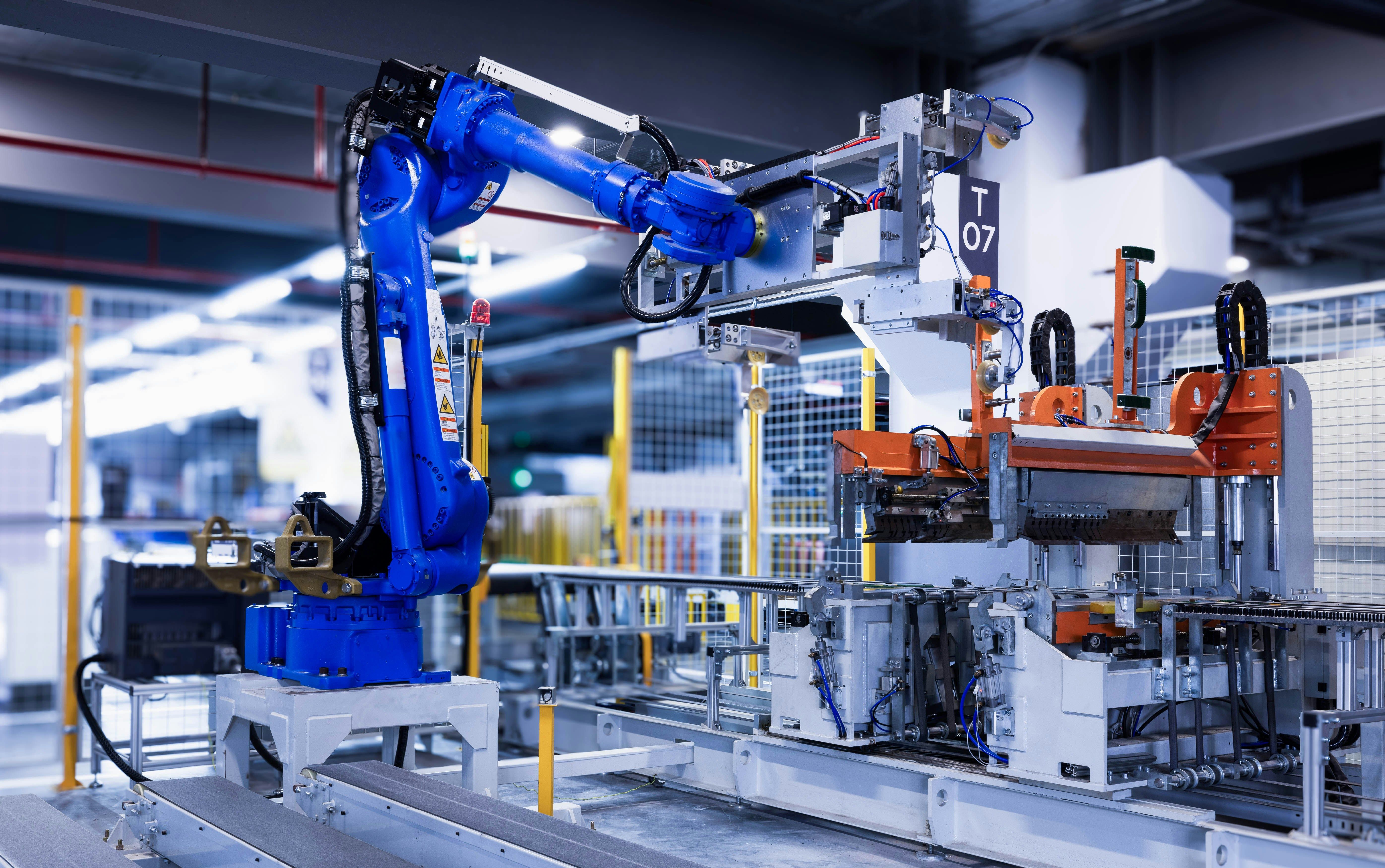 A blue industrial robot arm working with machinery on an assembly line.