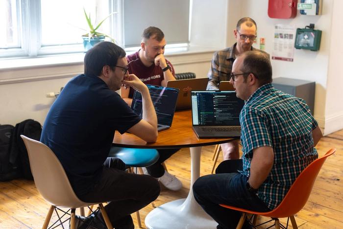 a group of men are sitting around a table with laptops .