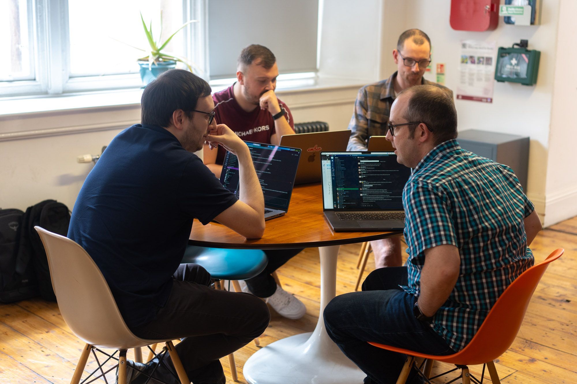 a group of men are sitting around a table with laptops .
