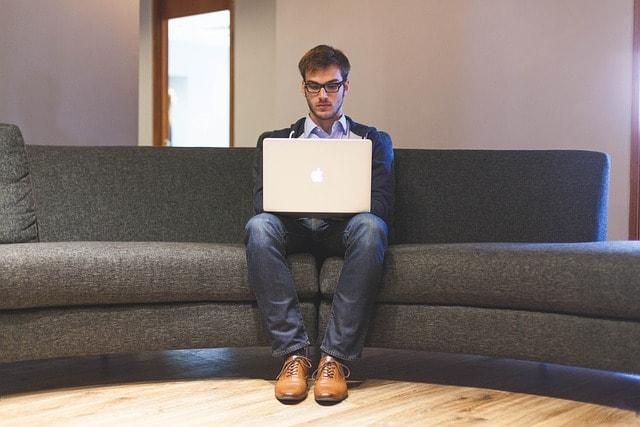 A man sitting on a couch using a laptop computer.