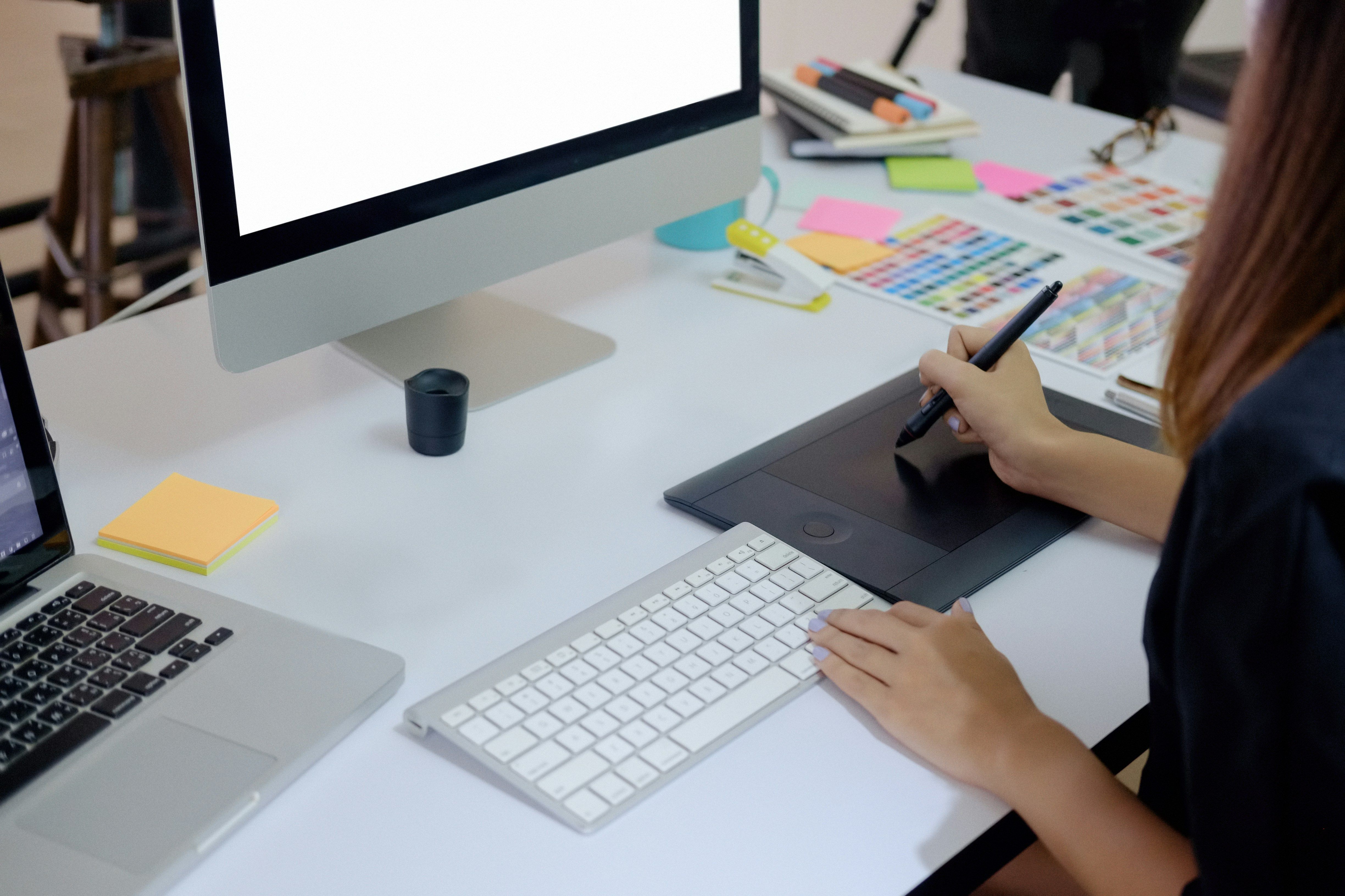 a woman is sitting at a desk using a graphic tablet and a computer .